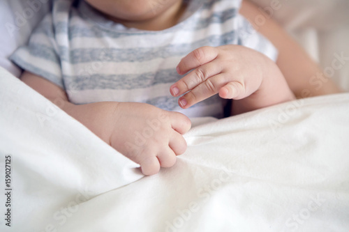 hand baby lying in bed and covered with a white blanket