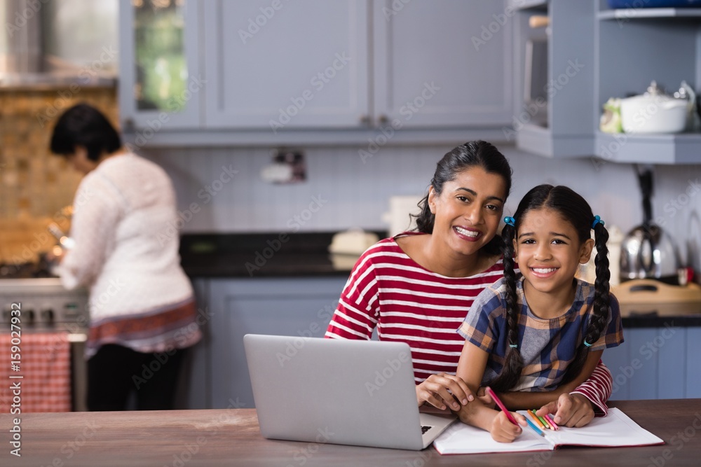 Portrait of smiling girl with mother studying in kitchen