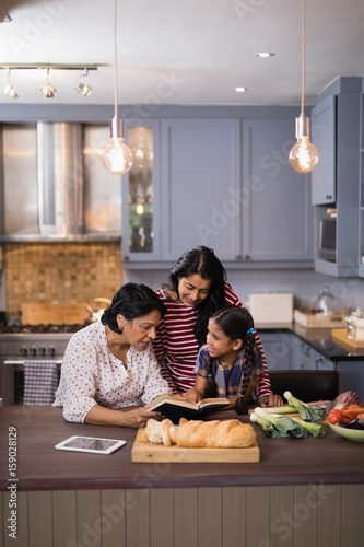 Multi-generation family reading book together in kitchen