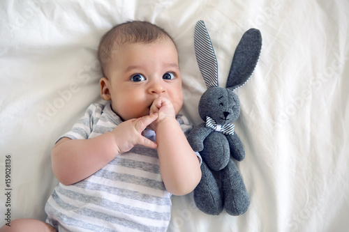 the child lies on his back on a big white bed with soft toy rabbit