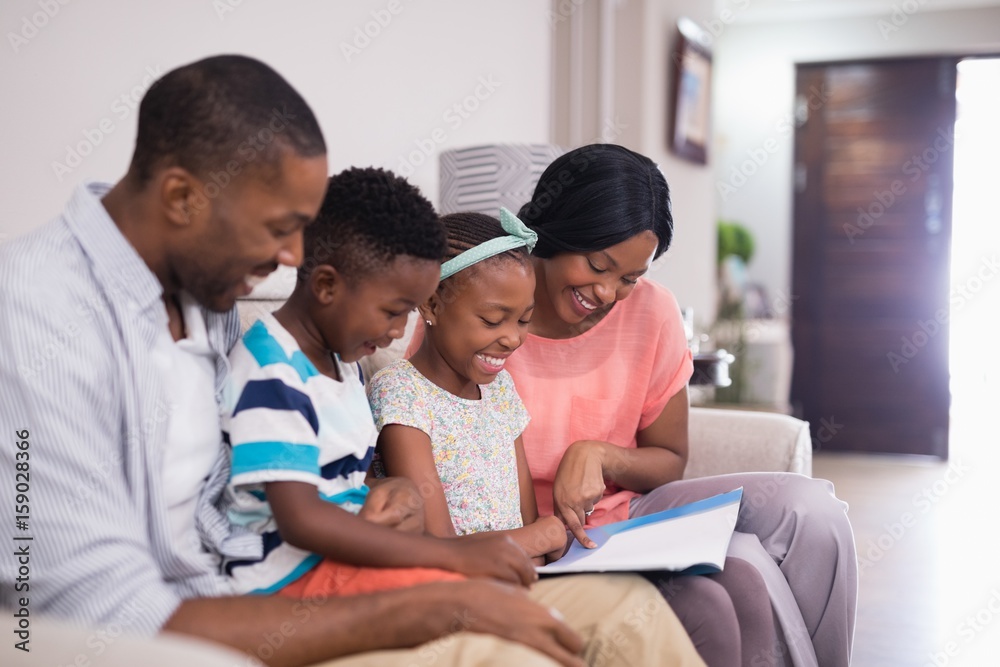 Smiling family reading magazine while sitting on sofa Smiling family reading magazine while sitting on sofa