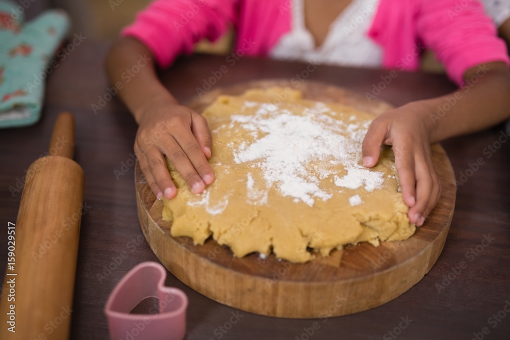 Mid section of girl touching dough in kitchen