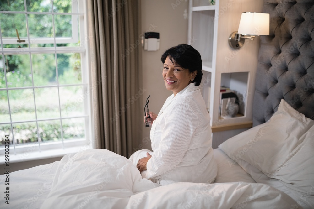 Smiling mature woman sitting in illuminated bedroom at home Smiling mature woman sitting in illuminated bedroom at home