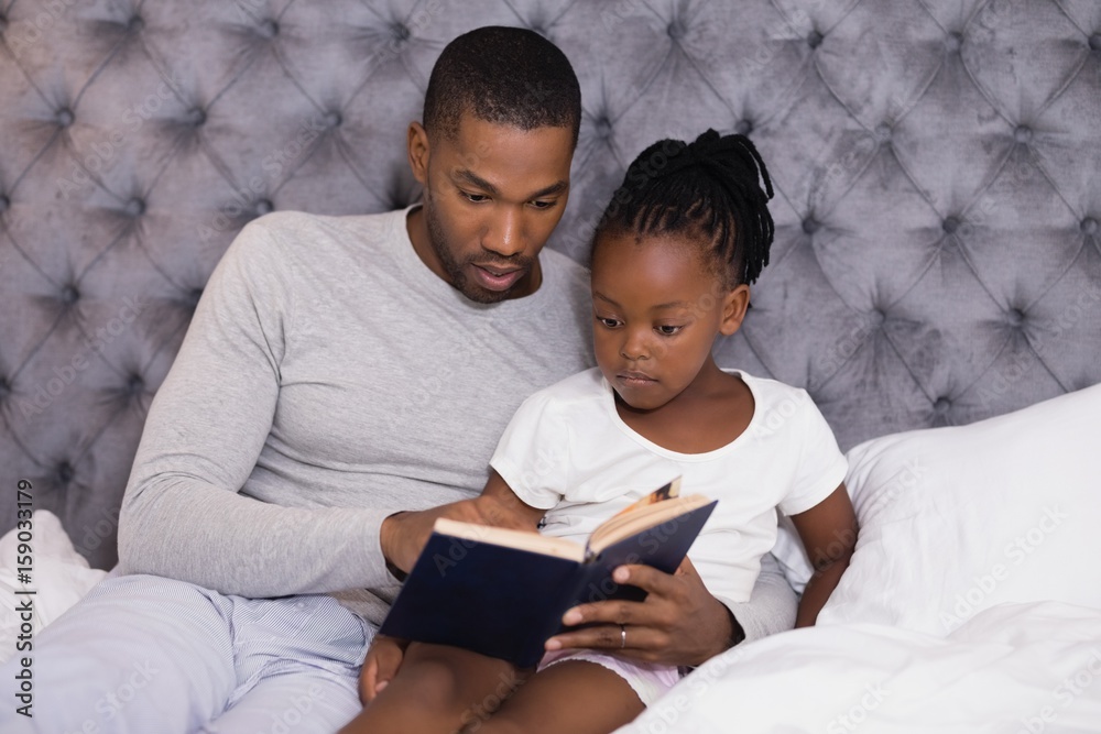 Fototapeta premium Man with daughter reading book on bed