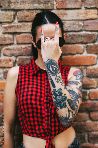 Young alternative woman with tattoos covering her face with a heavy metal sign photo