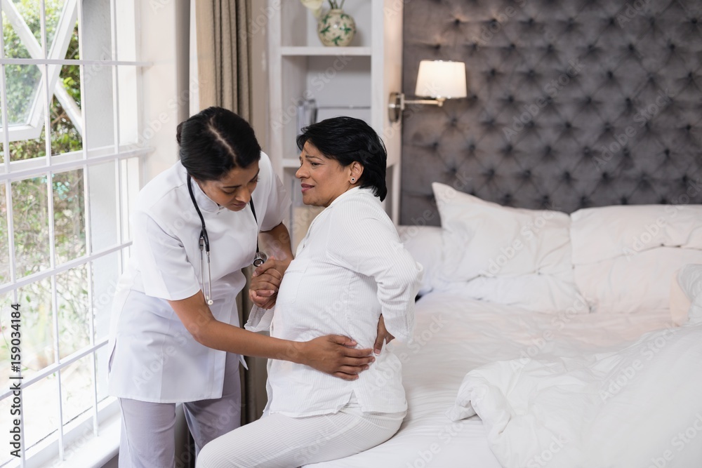 Nurse assisting female patient suffering with back pain on bed