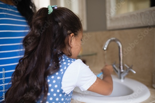 Girl with mother brushing teeth at bathroom sink