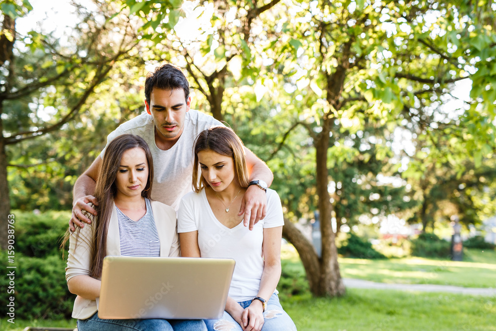 Amazig friends in nature sitting on bench and using laptop Amazig friends in nature sitting on bench and using laptop