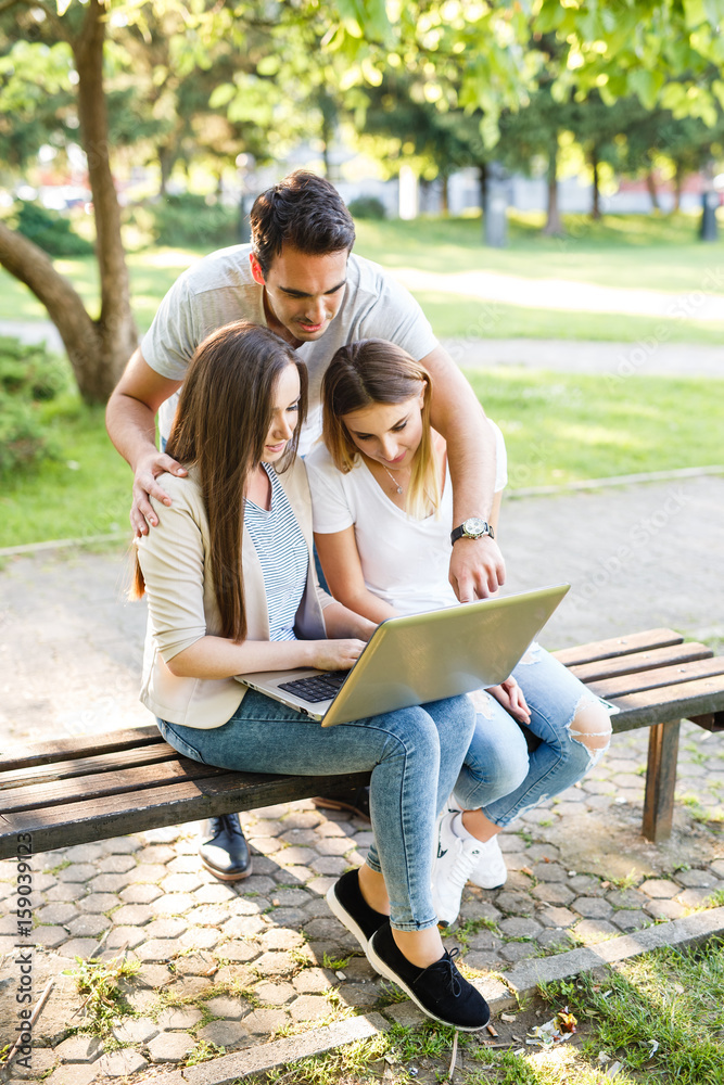 Three best friends in park enjoying the day and using laptop for browsing Three best friends in park enjoying the day and using laptop for browsing