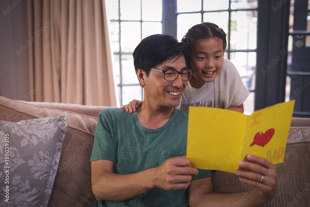 Obraz premium Father and daughter reading greeting card in living room