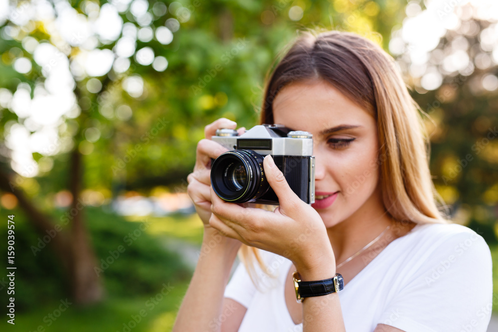 Cute girl on sunny day in park taking photos with analog camera