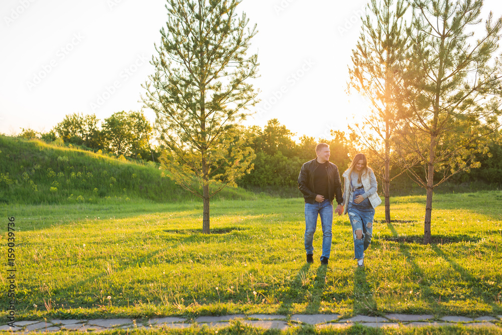 Pregnant woman with husband walking on meadow in the sunlight