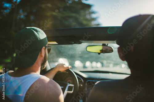 Two young men drive down a road in their convertible  photo