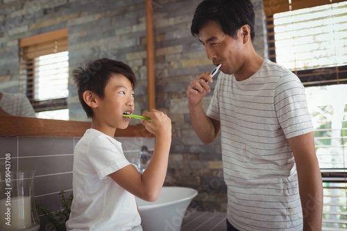 Father and son brushing teeth together in bathroom
