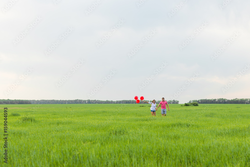 beautiful young couple hugging and kissing in a field with colored balloons