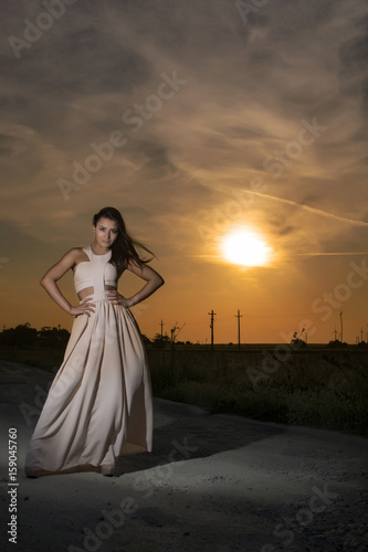 Young girl at sunset wearing a long white dress 