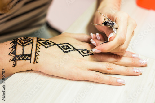 young woman mehendi artist painting henna on the hand photo