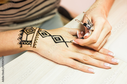 young woman mehendi artist painting henna on the hand photo