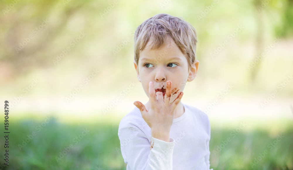 Cute little boy licking fingers while eating chocolate Cute little boy licking fingers while eating chocolate
