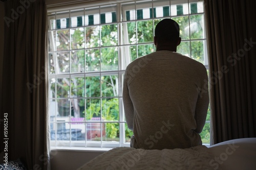 Rear view of man sitting on bed against window