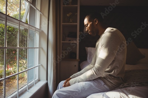 Cuadro en lienzo Side view of sad man sitting on bed by window