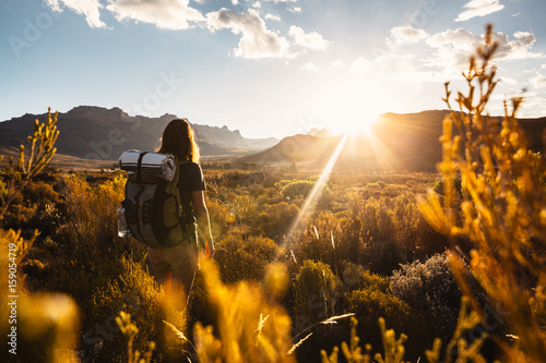 Woman hiking with a backpack through a mountainous valley at sunset photo