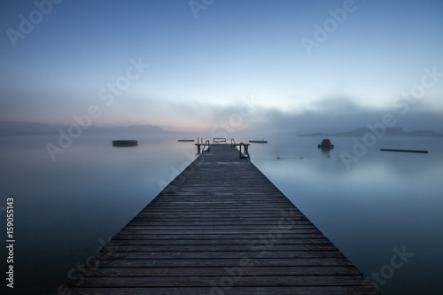 wooden dock on a lake in morning fog at sunrise photo