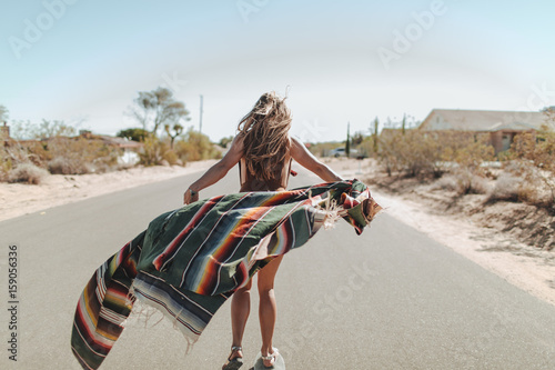 A carefree young woman stands in the middle of a desert road
