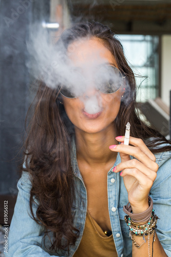 Beautiful tanned girl blowing cigarette smoke into the camera