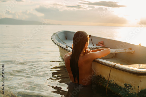 Girl in the sea leaning on a fishing boat