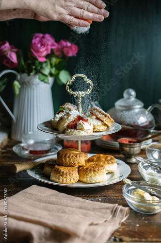 Jam and cream scones being dusted with icing sugar