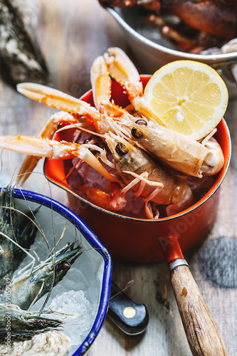 Langoustine and other shelled seafood in pots on a wooden surface with focus on the langoustine photo