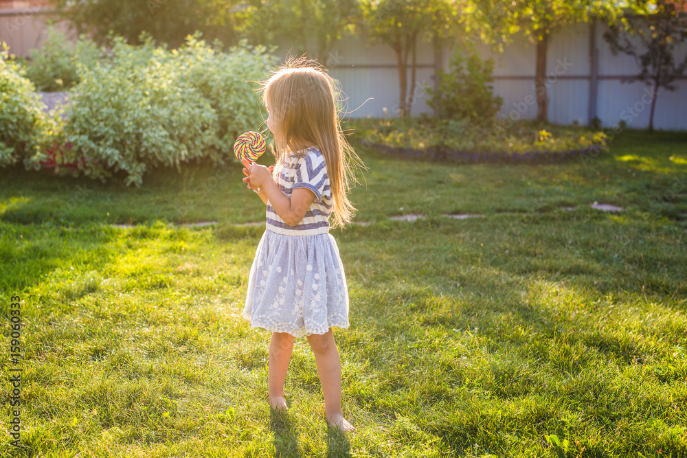 cute little girl eating a lollipop on the grass in summertime. cute little girl eating a lollipop on the grass in summertime.