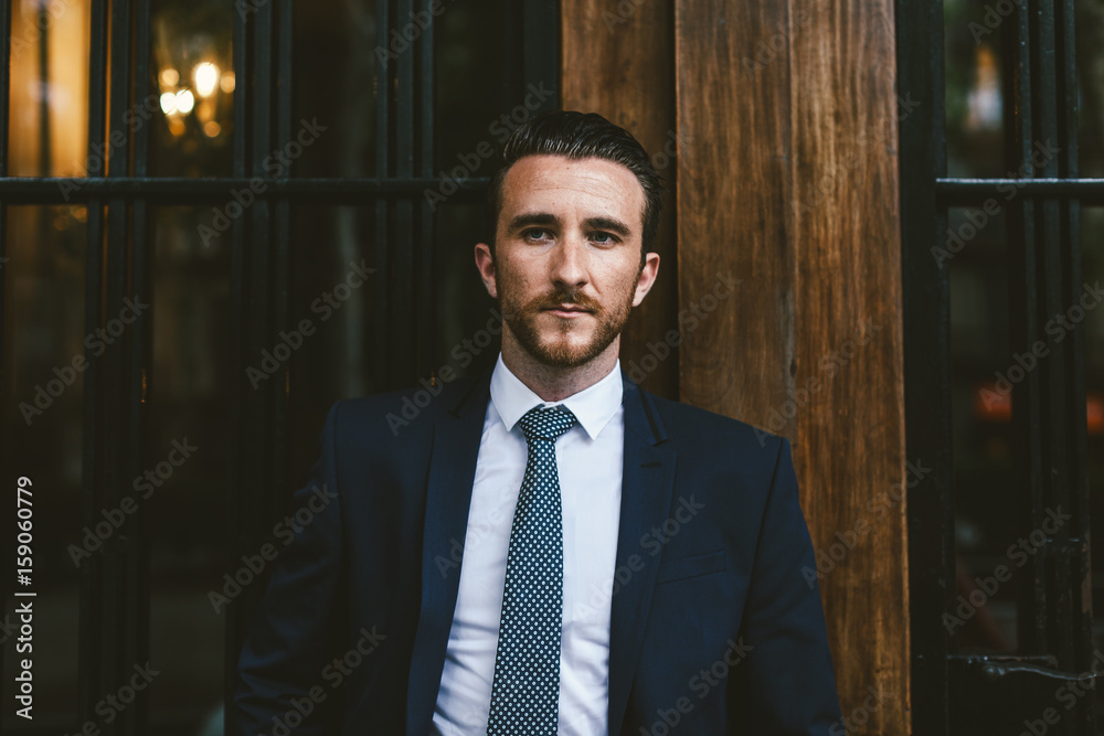 Young businessman wearing a suit standing in front of a wooden door Young businessman wearing a suit standing in front of a wooden door
