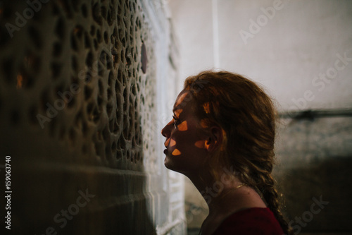 A young woman gazes through a carved stone screen in a historical building photo