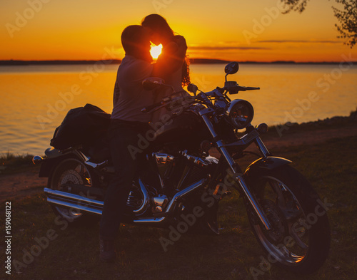 Obraz na plátně Two lovers with motorbike at sunset on the shore of the lake