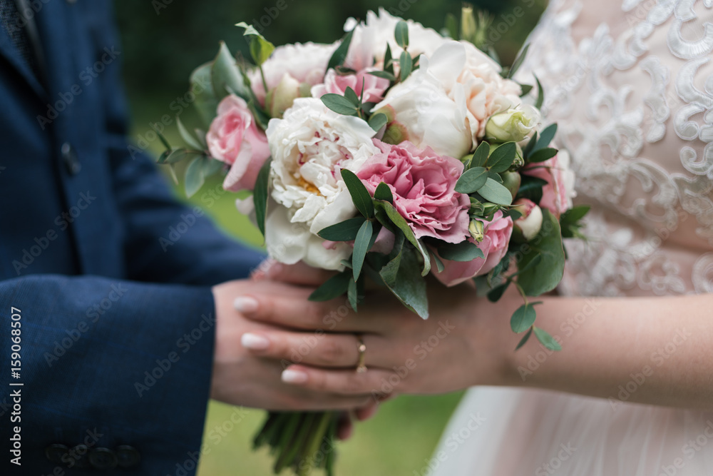 Beautiful wedding bouquet of white and pink peony in bride's and groom's hands in blur