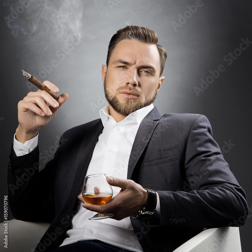 Man with cognac glass and cigar. Hair style, beard, suir and white shirt photo