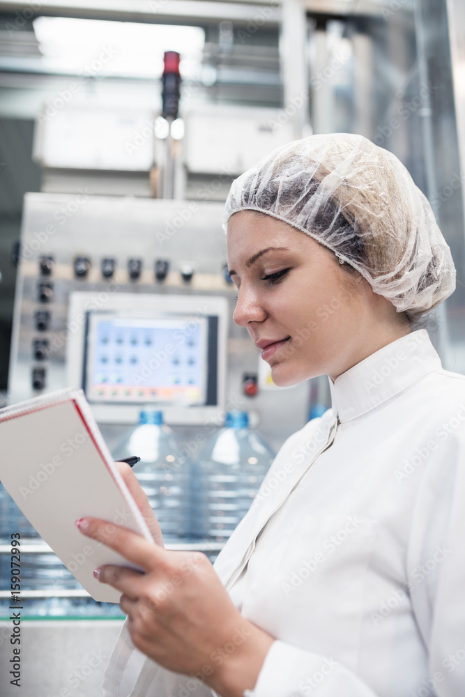 Young happy woman worker checking robotic line for bottling and packaging pure drinking water into bottles and canisters. Young happy woman worker checking robotic line for bottling and packaging pure drinking water into bottles and canisters.