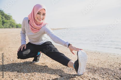asian sporty woman wearing hijab smiling while doing leg stretch