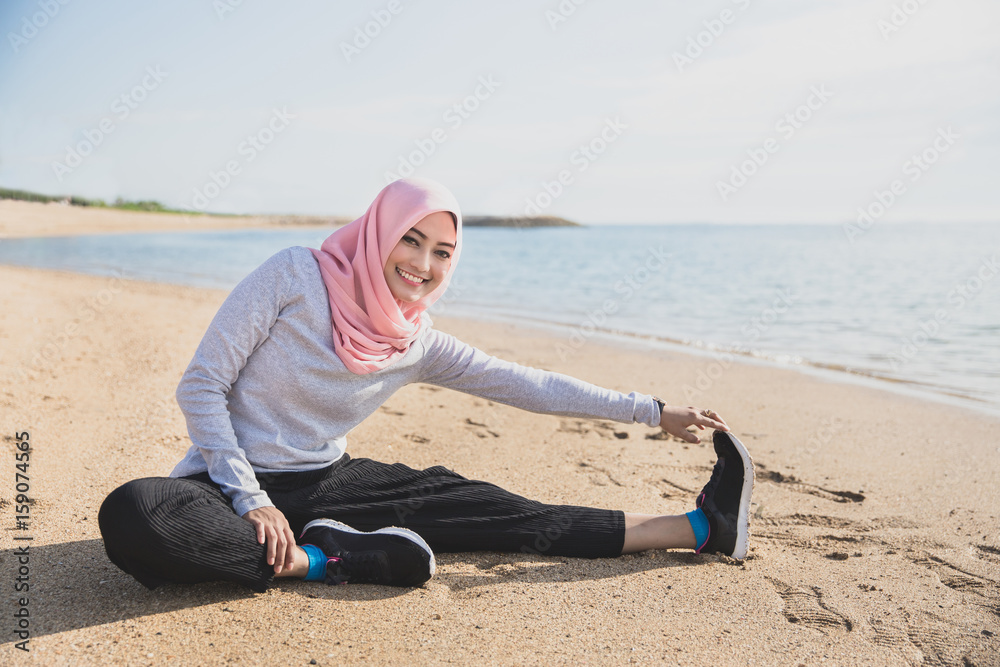 healthy sporty woman wearing hijab smiling while doing leg stret