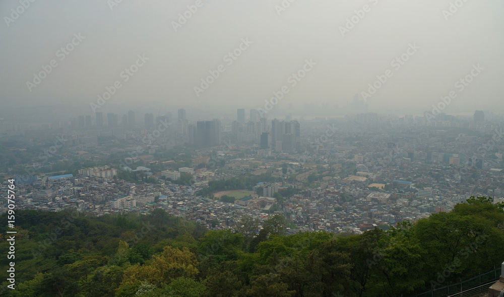 Smog over Seoul City. Skyline of downtown Seoul behind green vegetation with dense man-made smog obstructing the view. View from Namsan television tower, May 2017.