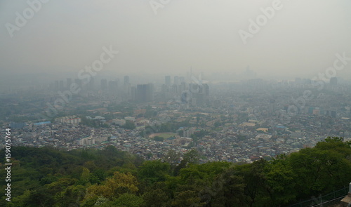 Smog over Seoul City. Skyline of downtown Seoul behind green vegetation with dense man-made smog obstructing the view. View from Namsan television tower, May 2017.
