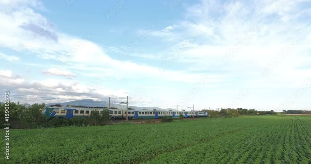 Passenger train is passing over the green meadow in the countryside. Passenger train is passing over the green meadow in the countryside.