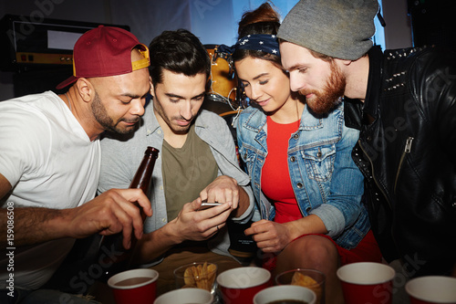 Group of friends hanging out at party  looking at smartphone screen of man showing something