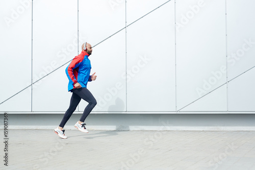 Active guy in sportswear running along wall of modern building