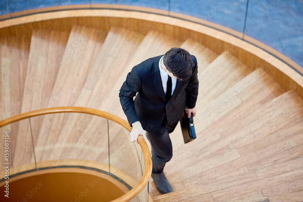 Young broker with briefcase moving upwards on staircase