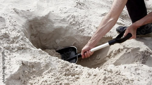 Man digging hole in white sand beach with shovel close up.