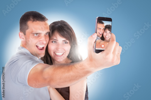 Close-up portrait of beautiful smiling couple hugging and looking at smartphone photo