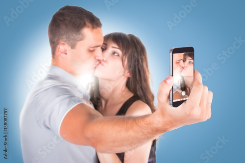 Close-up portrait of beautiful smiling couple hugging and looking at smartphone photo